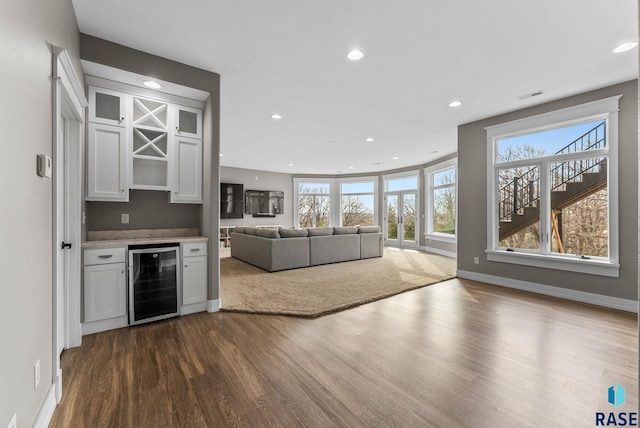 unfurnished living room featuring dark wood-style flooring, baseboards, a bar, wine cooler, and recessed lighting