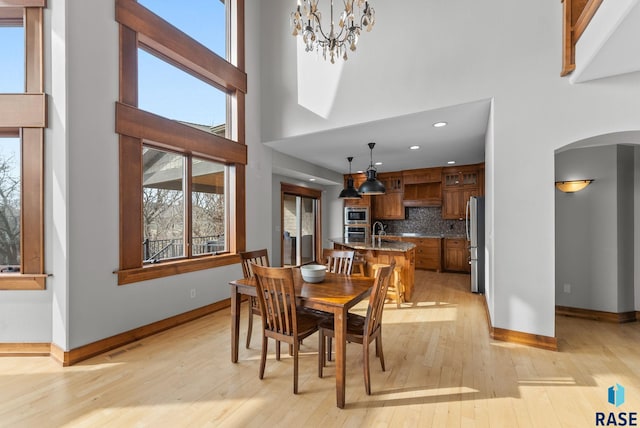 dining area with a towering ceiling, baseboards, light wood-type flooring, arched walkways, and a notable chandelier