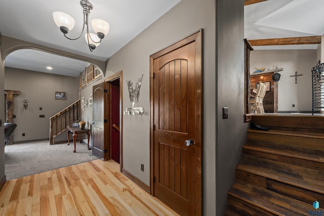 entryway featuring arched walkways, light wood-type flooring, baseboards, a chandelier, and stairs