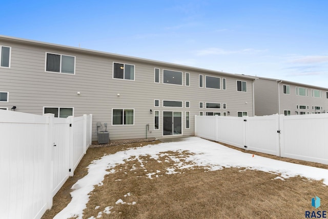 snow covered rear of property with cooling unit and a fenced backyard