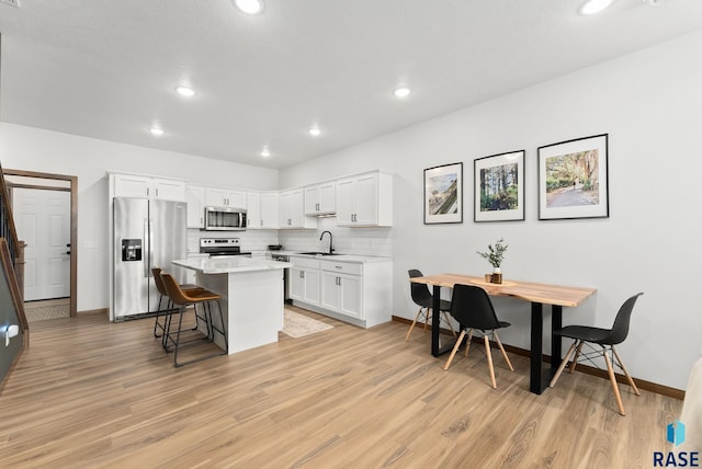 kitchen with a breakfast bar area, a sink, light countertops, light wood-style floors, and stainless steel appliances