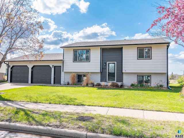 raised ranch featuring brick siding, an attached garage, driveway, and a front yard