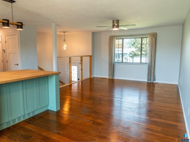 unfurnished living room featuring ceiling fan, baseboards, and dark wood-type flooring