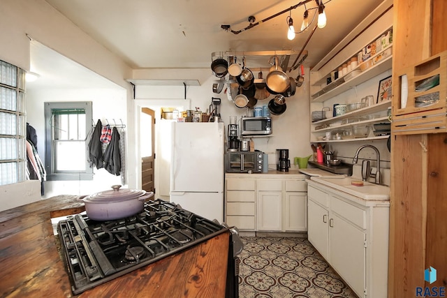 kitchen featuring white cabinets, open shelves, a sink, freestanding refrigerator, and stainless steel microwave