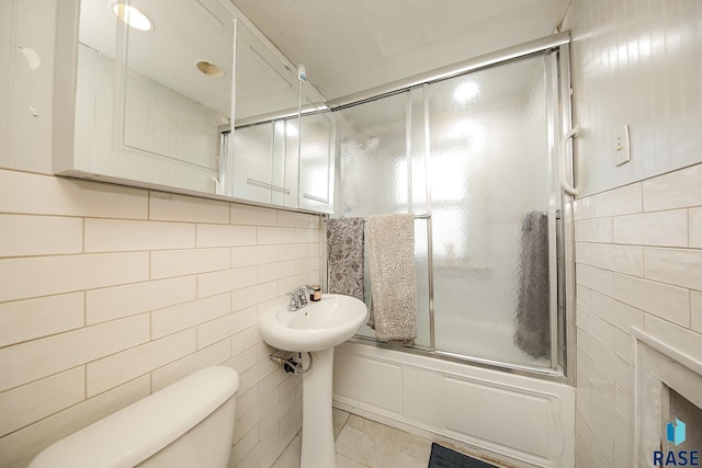full bath featuring enclosed tub / shower combo, toilet, and tile walls
