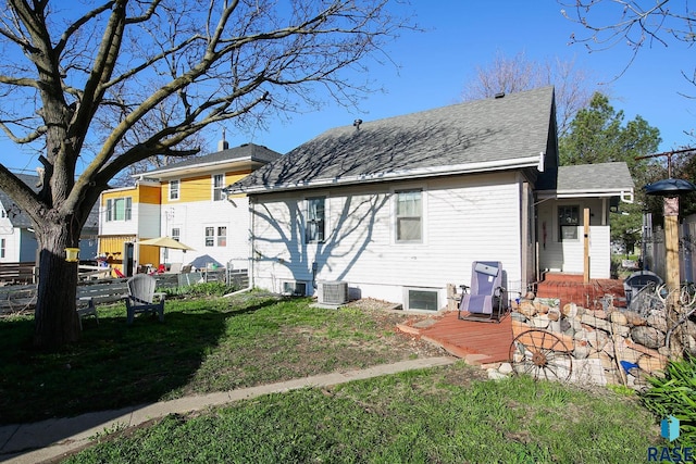 rear view of property with fence, roof with shingles, a deck, central air condition unit, and a yard