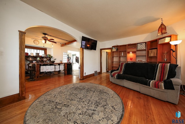 living room featuring baseboards, arched walkways, a ceiling fan, and wood finished floors
