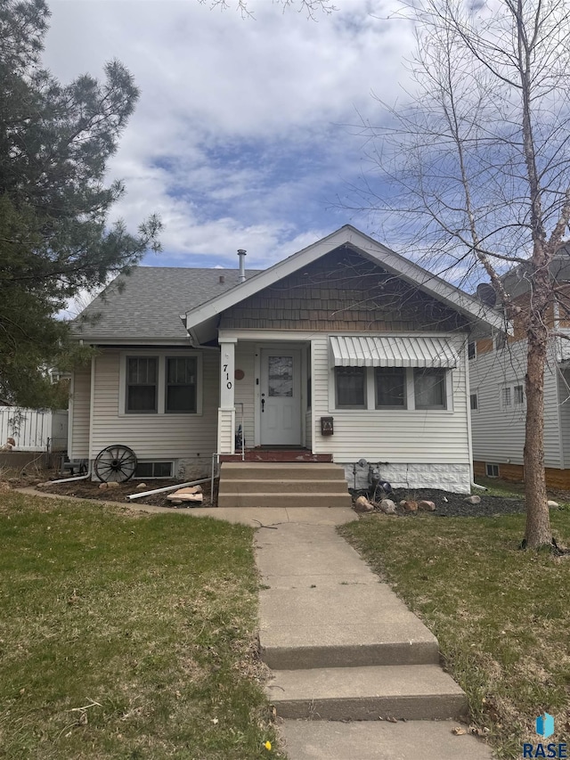 bungalow-style house featuring roof with shingles and a front lawn