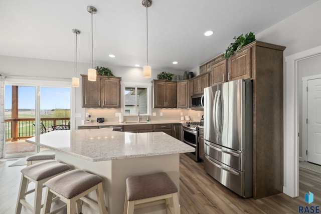 922 Johnson Creek Ct, Harrisburg, SD 57032 - kitchen with appliances with stainless steel finishes, a sink, dark wood-style floors, a kitchen bar, and backsplash