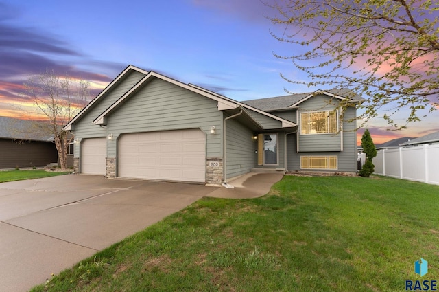 split level home featuring fence, a lawn, an attached garage, and concrete driveway