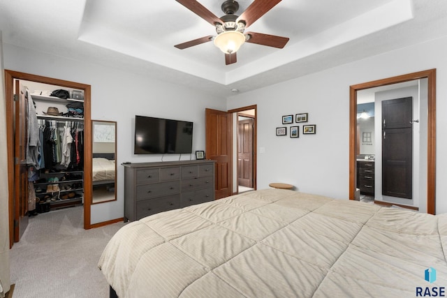 bedroom with carpet flooring, a walk in closet, a raised ceiling, ensuite bathroom, and a closet