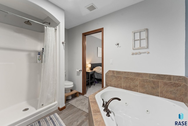 ensuite bathroom with toilet, a tub with jets, ensuite bathroom, wood finished floors, and visible vents