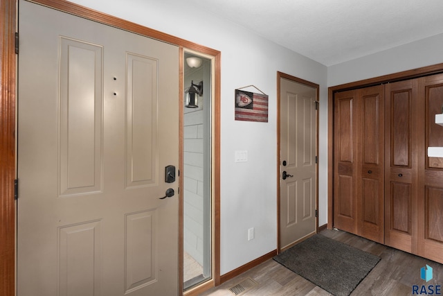 foyer entrance featuring baseboards, wood finished floors, and visible vents