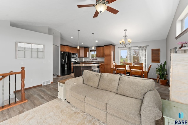 living area with a healthy amount of sunlight, dark wood finished floors, baseboards, ceiling fan with notable chandelier, and lofted ceiling