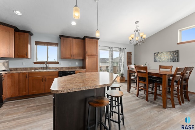 kitchen with a sink, a breakfast bar area, brown cabinets, and light wood-style flooring