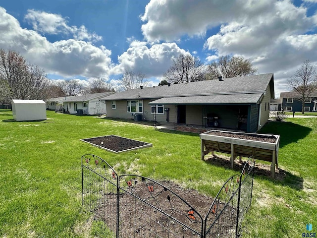 back of property featuring roof with shingles, an outdoor structure, a yard, and a garden