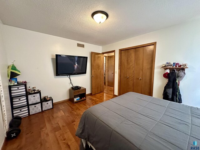 bedroom featuring a textured ceiling, baseboards, wood finished floors, visible vents, and a closet