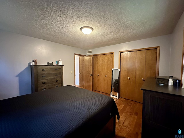 bedroom with visible vents, a textured ceiling, multiple closets, and wood finished floors