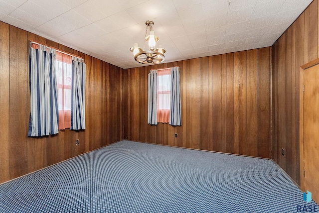 carpeted empty room with wood walls and a notable chandelier