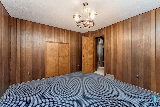 carpeted spare room featuring visible vents, wood walls, and a notable chandelier
