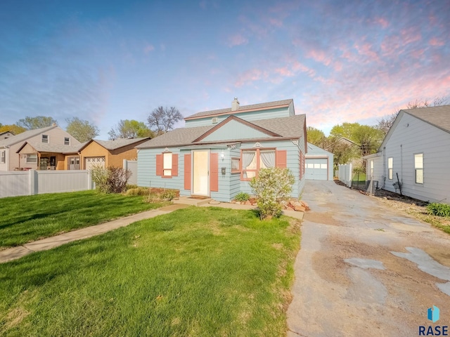 bungalow featuring fence, a detached garage, and a lawn