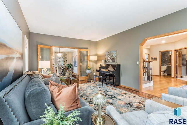 living area with arched walkways, baseboards, and light wood-style floors