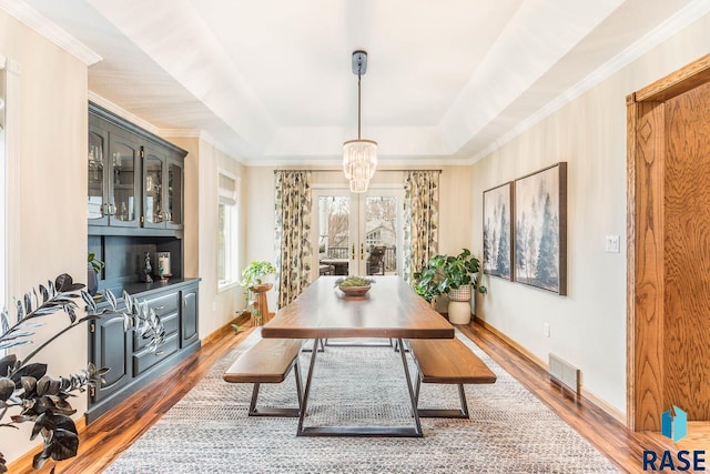 dining space featuring visible vents, wood finished floors, baseboards, a notable chandelier, and a tray ceiling