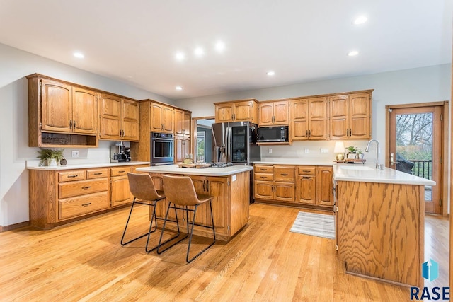 kitchen with stainless steel appliances, a kitchen breakfast bar, a sink, and light wood-style floors