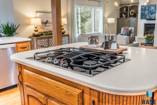 room details with brown cabinets, black gas stovetop, dishwasher, light countertops, and a fireplace with raised hearth
