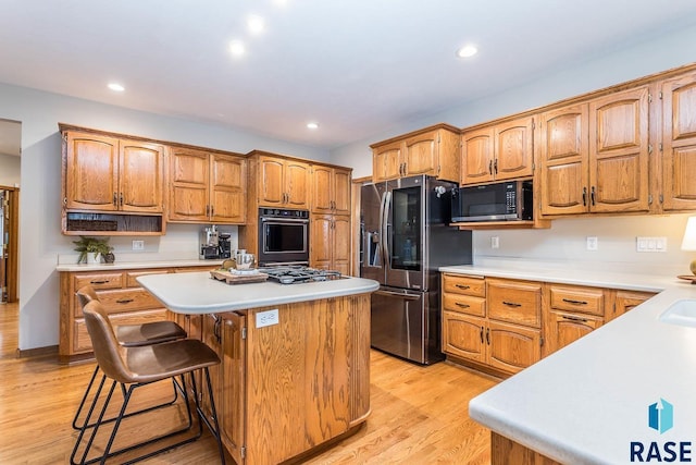 kitchen with light countertops, appliances with stainless steel finishes, a kitchen island, and light wood finished floors