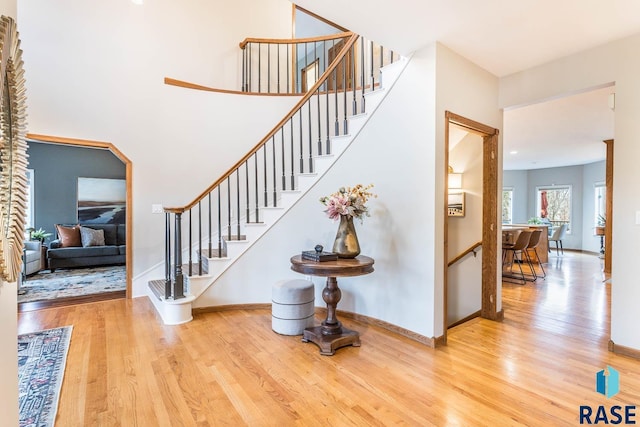 staircase featuring arched walkways, baseboards, and wood finished floors