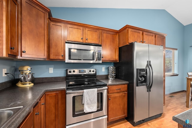 kitchen featuring dark countertops, appliances with stainless steel finishes, brown cabinets, and lofted ceiling