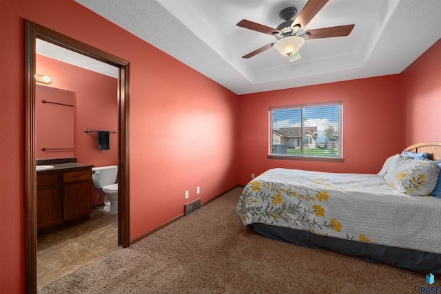 carpeted bedroom featuring visible vents, a ceiling fan, ensuite bath, and a tray ceiling