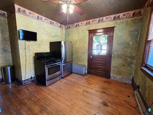 kitchen featuring a ceiling fan, appliances with stainless steel finishes, baseboard heating, hardwood / wood-style flooring, and radiator