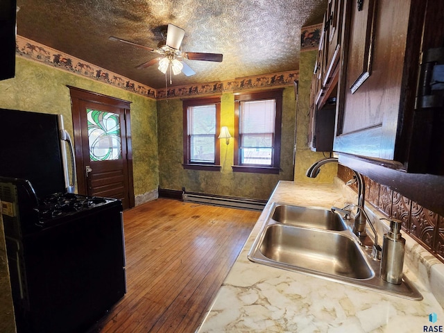 kitchen with ceiling fan, black gas stove, a sink, a baseboard radiator, and wood-type flooring