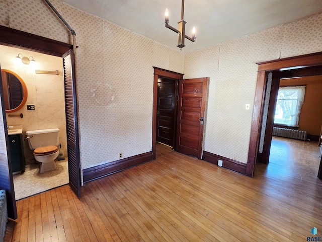 interior space with wallpapered walls, a notable chandelier, radiator heating unit, and hardwood / wood-style flooring