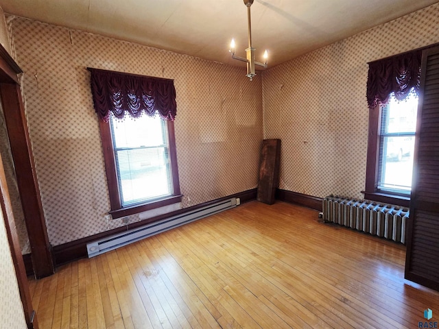 spare room with wallpapered walls, hardwood / wood-style floors, radiator, and a baseboard radiator