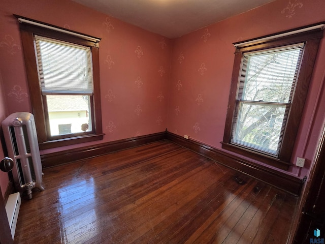 empty room featuring a baseboard heating unit, radiator heating unit, a healthy amount of sunlight, and hardwood / wood-style floors