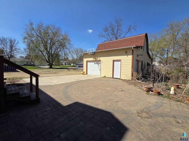 view of side of property with an attached garage, a shingled roof, an outbuilding, and concrete driveway