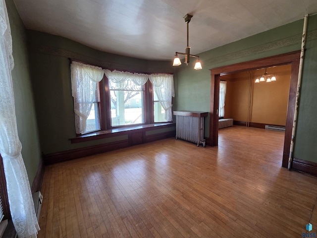 unfurnished dining area featuring visible vents, radiator heating unit, a notable chandelier, and hardwood / wood-style floors