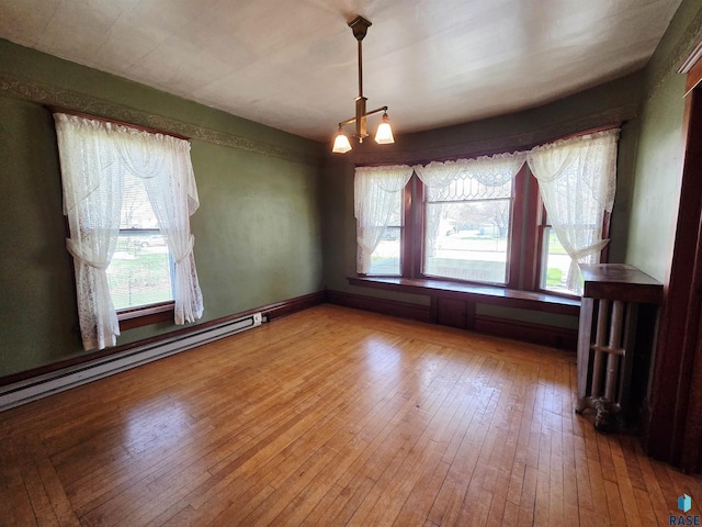 unfurnished dining area with plenty of natural light, a baseboard radiator, and hardwood / wood-style flooring