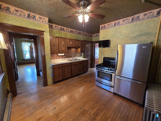 kitchen featuring a sink, light countertops, stainless steel appliances, a ceiling fan, and light wood-type flooring