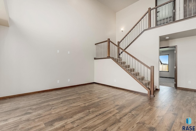 5714 S Woodlily Ave, Sioux Falls, SD 57108 - unfurnished living room featuring stairs, baseboards, a towering ceiling, and wood finished floors