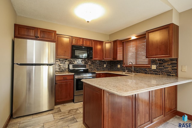 kitchen with appliances with stainless steel finishes, a peninsula, backsplash, a sink, and brown cabinetry