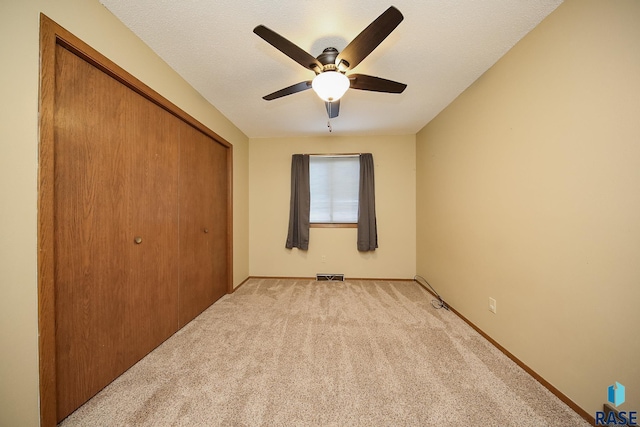 unfurnished bedroom with a closet, visible vents, light carpet, a ceiling fan, and baseboards