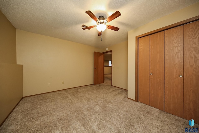 unfurnished bedroom featuring light colored carpet, a closet, a ceiling fan, and a textured ceiling