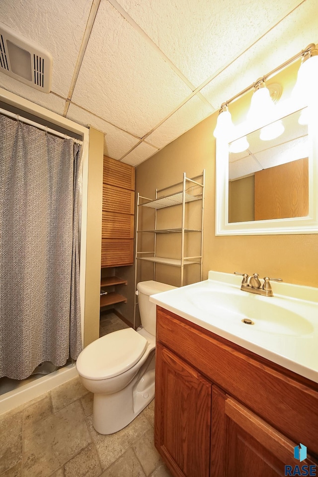 full bathroom featuring toilet, curtained shower, vanity, a drop ceiling, and stone finish flooring