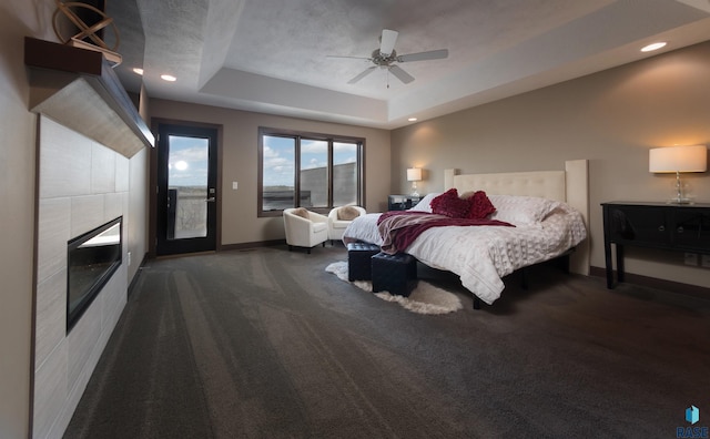 carpeted bedroom featuring recessed lighting, a raised ceiling, baseboards, a tiled fireplace, and access to exterior