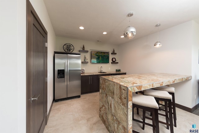 kitchen featuring a sink, a kitchen breakfast bar, stainless steel refrigerator with ice dispenser, recessed lighting, and baseboards