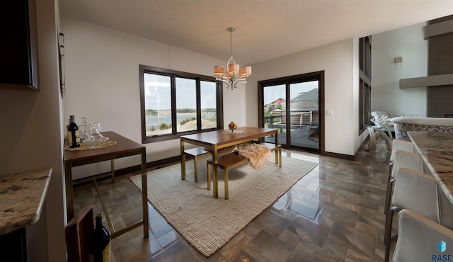 dining area with a chandelier, baseboards, and stone tile flooring
